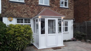 White uPVC entrance porch with tiled hip roof on a tile-hung house