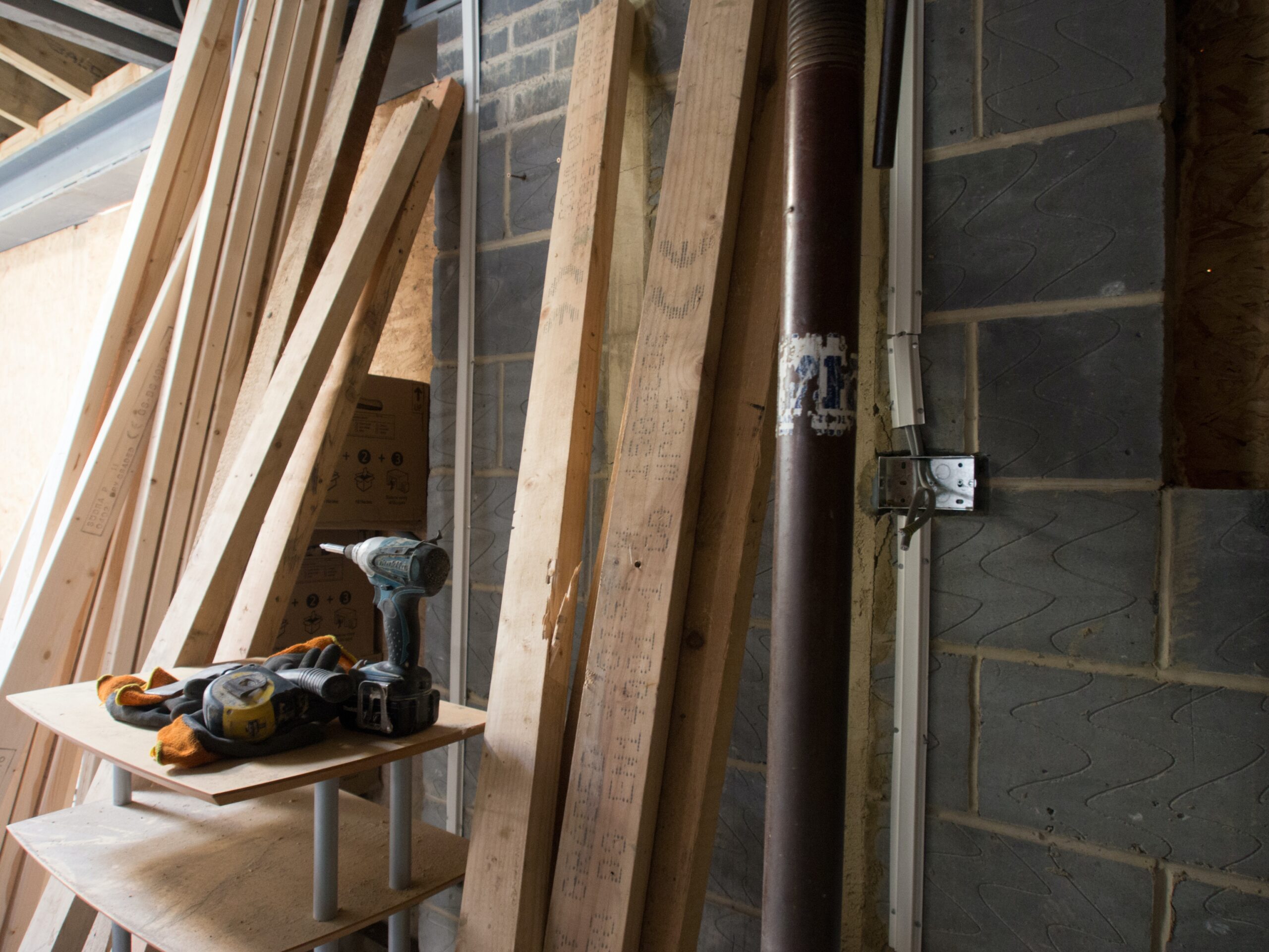 Timber planks, cordless drill and work gloves beside a block wall